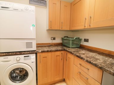 A laundry room with a washing machine dryer wooden cabinets and a green laundry basket on the counter at Birchenhayes in St Dominick