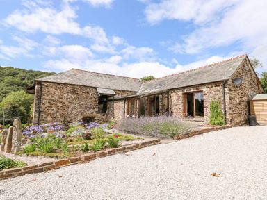 A stone house with slate roof surrounded by flower beds and gravel driveway at Birchenhayes in St Dominick