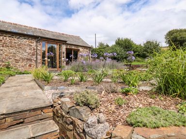 A stone house with a garden featuring stone steps plants and purple flowers at Birchenhayes in St Dominick