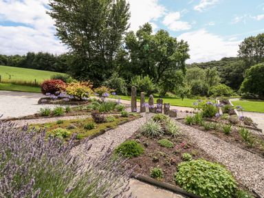 A garden with flower beds and standing stones surrounded by trees at Birchenhayes in St Dominick
