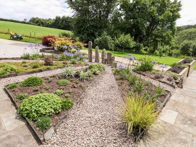 A garden with flower beds gravel paths stone pillars and green lawn at Birchenhayes in St Dominick