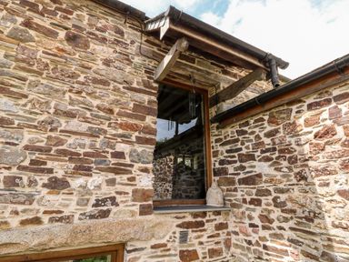 A stone exterior wall with a wooden framed window and a small statue at Birchenhayes in St Dominick