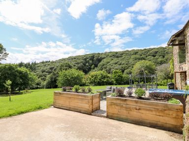 A garden with wooden planters a seating area a hot tub and a metal gazebo near a stone building at Birchenhayes in St Dominick