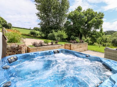 An outdoor hot tub with bubbling water in a garden with trees and greenery at Birchenhayes in St Dominick