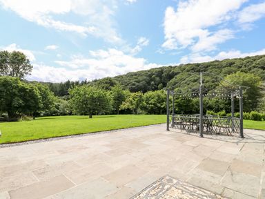 An outdoor patio area with a metal gazebo and chairs surrounded by grass and trees at Birchenhayes in St Dominick