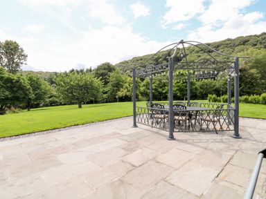 A metal gazebo with outdoor furniture on a patio surrounded by grass and trees at Birchenhayes in St Dominick