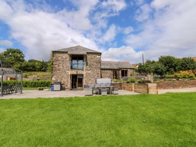 A stone house with patio furniture and garden beds on a lawn at Birchenhayes in St Dominick