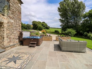 An outdoor patio area with a hot tub and wicker seating near a stone building at Birchenhayes in St Dominick