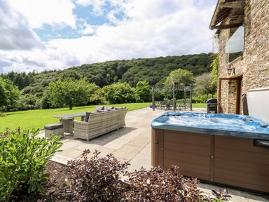 An outdoor patio with a hot tub sofa and table with chairs and a gazebo in a garden at Birchenhayes in St Dominick