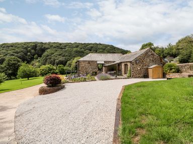 A stone barn house with gravel driveway and green lawn surrounded by trees at Birchenhayes St Dominick