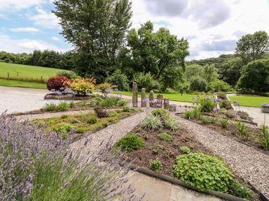 A garden with flower beds gravel paths stone pillars and trees at Birchenhayes in St Dominick