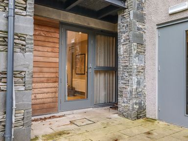 An outdoor entrance area with stone and wood walls and a glass door at Bruach in Backbarrow