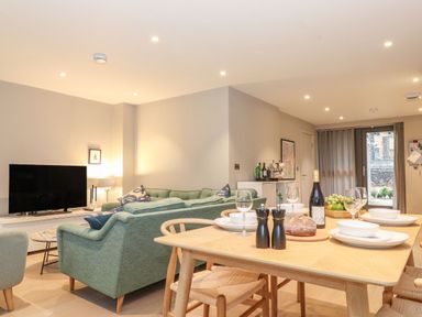 A dining table set with glasses and plates next to a living room with green sofas and a TV at Bruach in Backbarrow