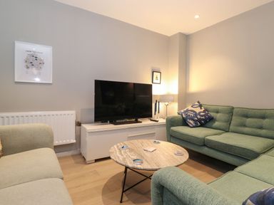 A living room with green sofas a round coffee table and a television on a white stand at Bruach in Backbarrow
