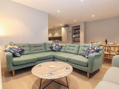 A living room with a green sectional sofa blue patterned pillows and a round wooden coffee table at Bruach in Backbarrow