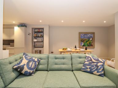 A living room with a green sofa and blue patterned cushions facing a dining table with plates glasses and a bottle of wine at Bruach in Backbarrow