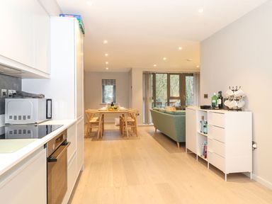 A kitchen with a microwave and oven a dining table with chairs and a living area with a sofa and cabinet at Bruach in Backbarrow