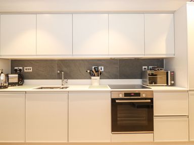 A kitchen with white cabinets a double sink a built in oven a microwave toaster kettle and utensils at Bruach in Backbarrow