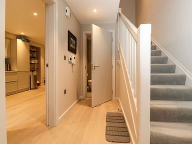 A hallway with wooden floor mats stairs with carpet and an open door leading to a bathroom at Bruach in Backbarrow