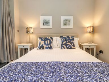 A bedroom with a bed with blue patterned cushions and cover with two bedside tables and lamps at Bruach in Backbarrow