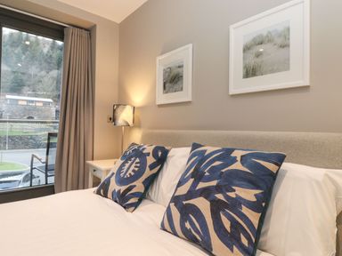 A bedroom with a bed with patterned pillows a bedside table with a lamp and framed artwork on the wall at Bruach in Backbarrow