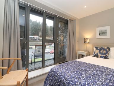 A bedroom with a bed next to a nightstand and lamp and glass doors leading to a balcony at Bruach in Backbarrow