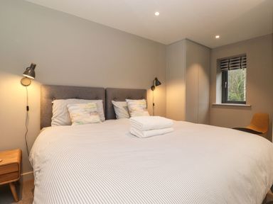 A bedroom with a double bed with pillows and towels a wooden nightstand and a chair at Bruach in Backbarrow