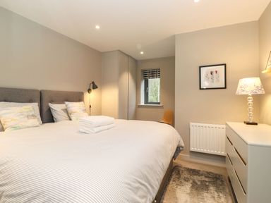 A bedroom with a bed table lamp chest of drawers framed wall art and a window at Bruach in Backbarrow