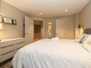 A bedroom with a bed with folded towels on top and a white dresser with framed pictures on a shelf at Bruach in Backbarrow