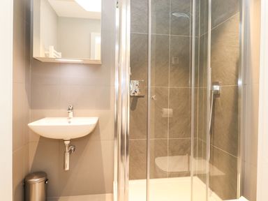 A bathroom with a wall-mounted sink mirror trash can and a glass shower enclosure at Bruach in Backbarrow
