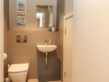 A small bathroom with a toilet a sink a mirror and two framed pictures on the wall at Bruach in Backbarrow