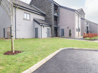 A multi story modern building with grey walls and windows surrounded by grass and a tree at Bruach in Backbarrow
