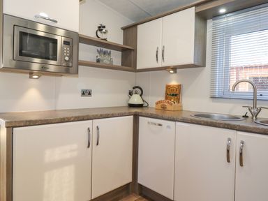 A kitchen with white cabinets a microwave kettle sink and a window with blinds at Pegasus Felmoor Park