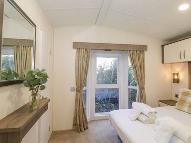 A bedroom with a bed towel set and checked pillows near a window with curtains and a wall mirror on a shelf at Pegasus in Felmoor Park