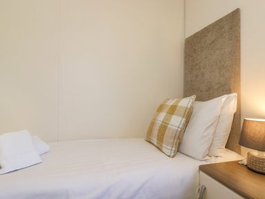 A single bed with a headboard pillows a checkered cushion and a bedside table with a lamp at Pegasus Felmoor Park