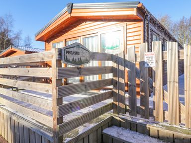 A wooden cabin with a fenced deck and a caution sign about slippery decking at Pegasus in Felmoor Park