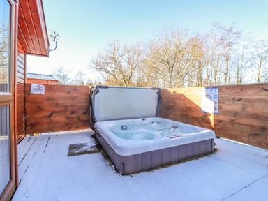 An outdoor hot tub on a snow-covered wooden deck with wooden fencing and trees in the background at Pegasus in Felmoor Park