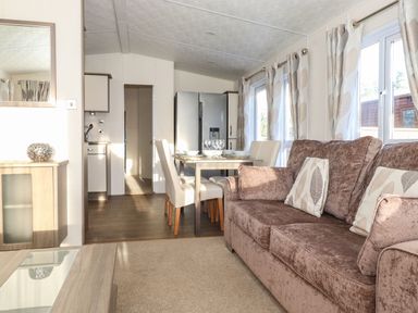 A living area with a brown sofa and dining table with chairs near kitchen and windows at Hercules in Felmoor Park