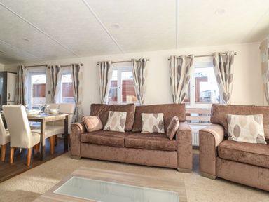 A living room with brown sofas and patterned curtains next to a dining table with chairs at Hercules in Felmoor Park