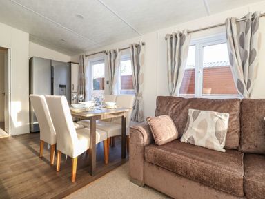A dining area with a wooden table set with white dishes and glasses next to a brown sofa and windows with patterned curtains at Hercules in Felmoor Park