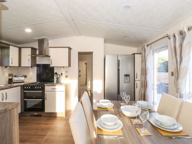 A dining table set with white dishes and glasses in a kitchen with a stove refrigerator and curtains at Hercules in Felmoor Park