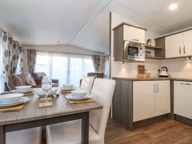 A dining area with set table and white chairs next to a kitchen with cabinets and a microwave at Hercules in Felmoor Park