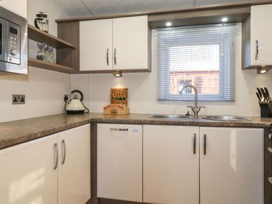A kitchen with a kettle a microwave a knife block a double sink and a window with blinds at Hercules in Felmoor Park