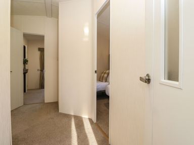A hallway with beige carpet and cream walls showing doors leading to a bedroom and another room with a vase of flowers at Hercules in Felmoor Park