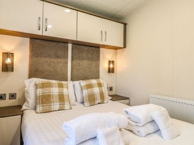 A bedroom with a double bed with plaid cushions and white towels on it at Hercules in Felmoor Park