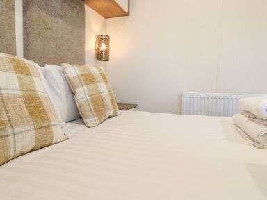 A bed with white linens and plaid pillows next to a nightstand and wall light at Hercules in Felmoor Park