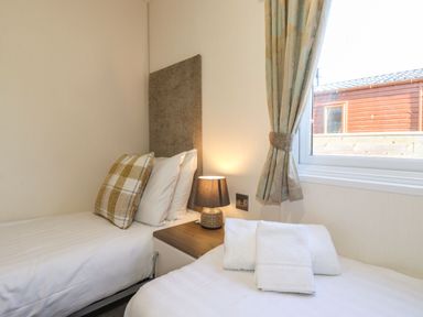 A small bedroom with two single beds a bedside table a lamp and a window at Hercules in Felmoor Park