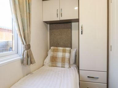 A small bedroom with a single bed beside a window with curtains and built-in cabinets at Hercules in Felmoor Park
