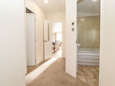 A hallway with carpeted floor leading to a bathroom with a bathtub and a room with a dining table and chairs at Hercules in Felmoor Park