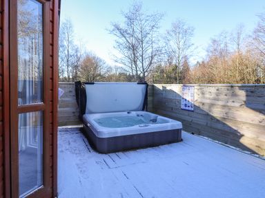 An outdoor hot tub on a snow-covered wooden deck surrounded by a wooden fence with trees in the background at Hercules in Felmoor Park